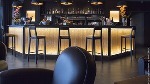 Una zona de bar con mostrador de madera, taburetes negros y lámparas colgantes.