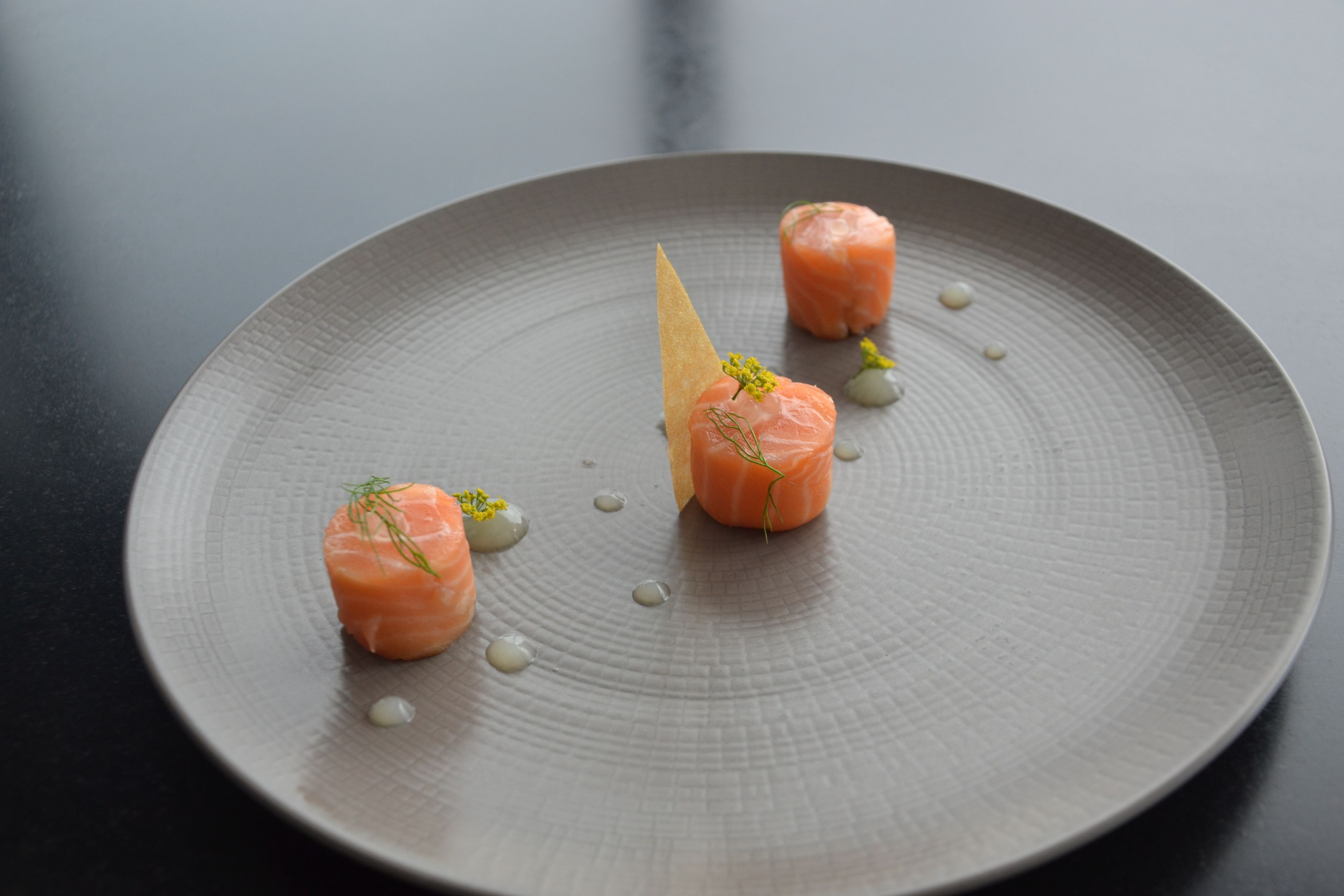 Une assiette contenant trois morceaux de saumon et une garniture triangulaire.