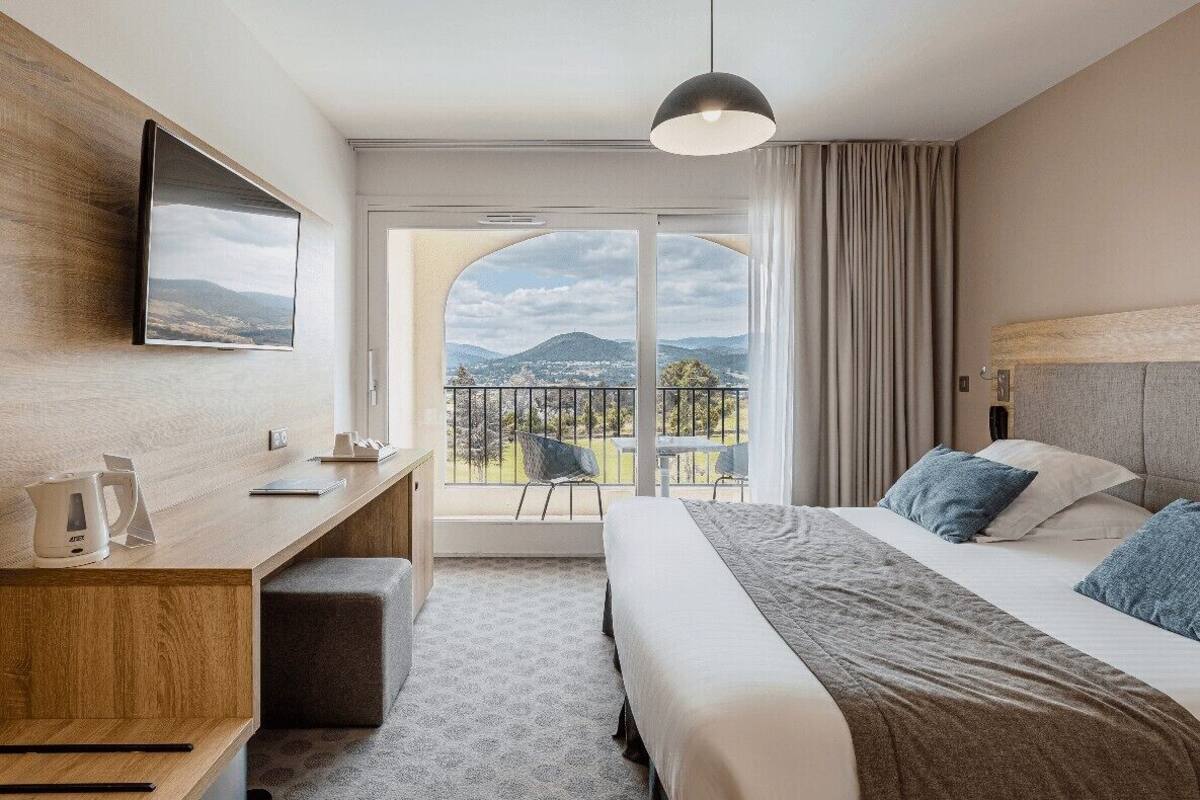Habitación de hotel con cama, escritorio, televisión y balcón con vistas.