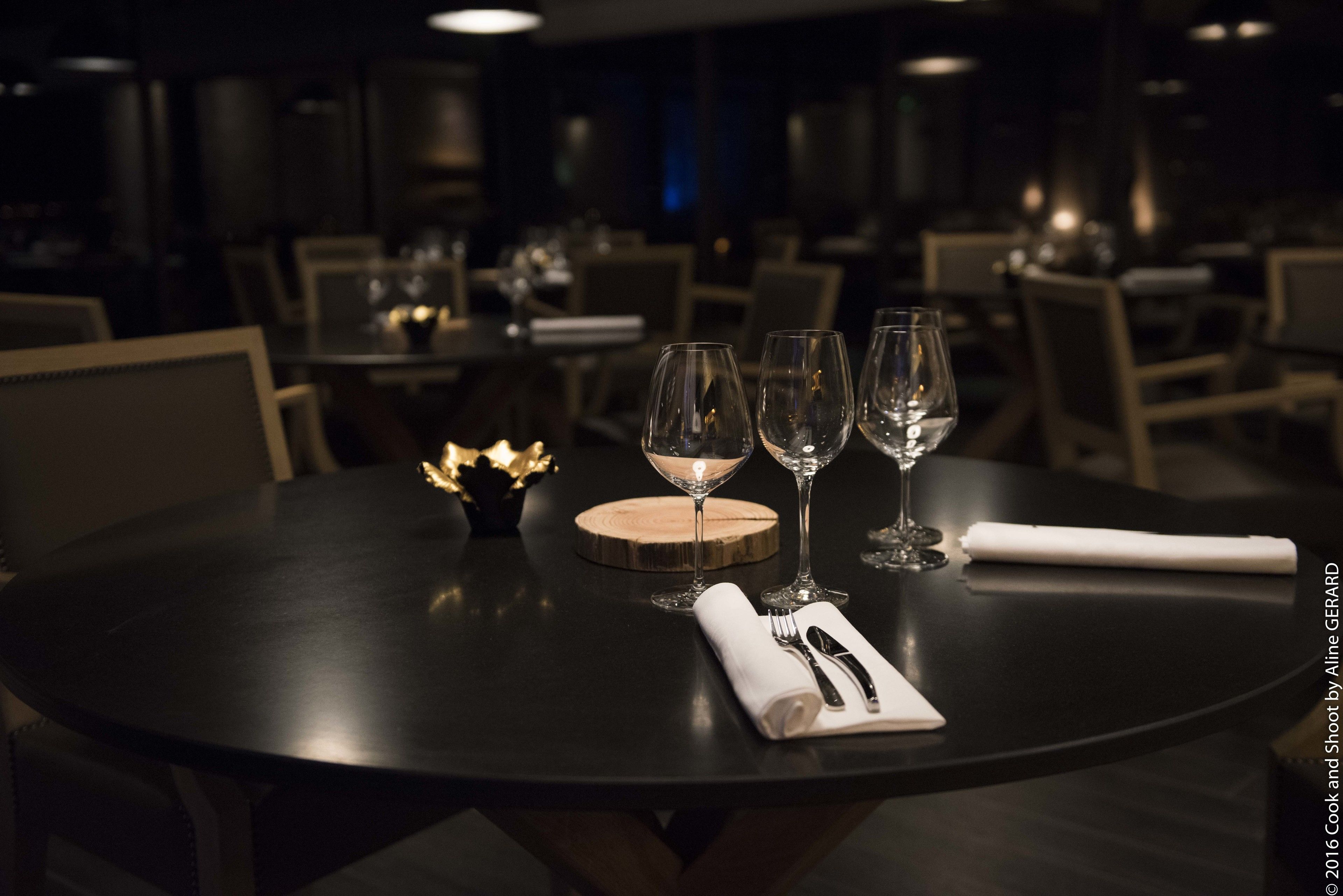 Une table à manger dressée avec trois verres à vin, un sous-verre en bois, une serviette pliée et des couverts.