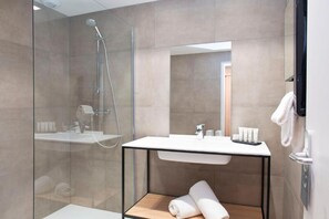 Een moderne badkamer met een glazen douchecabine, een wit wastafelmeubel met een zwart frame en een houten plank met handdoeken.