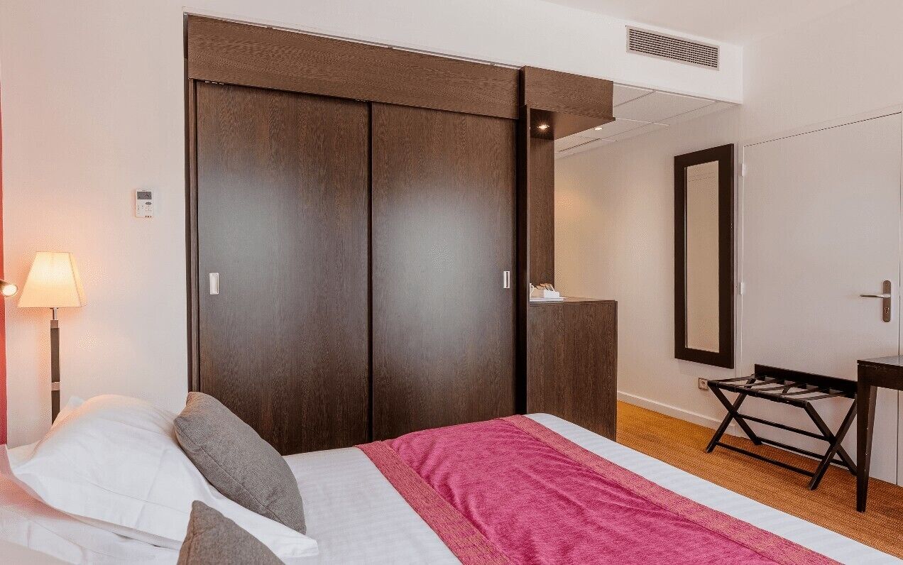 A bedroom with a bed, a wardrobe, a desk, and a mirror.