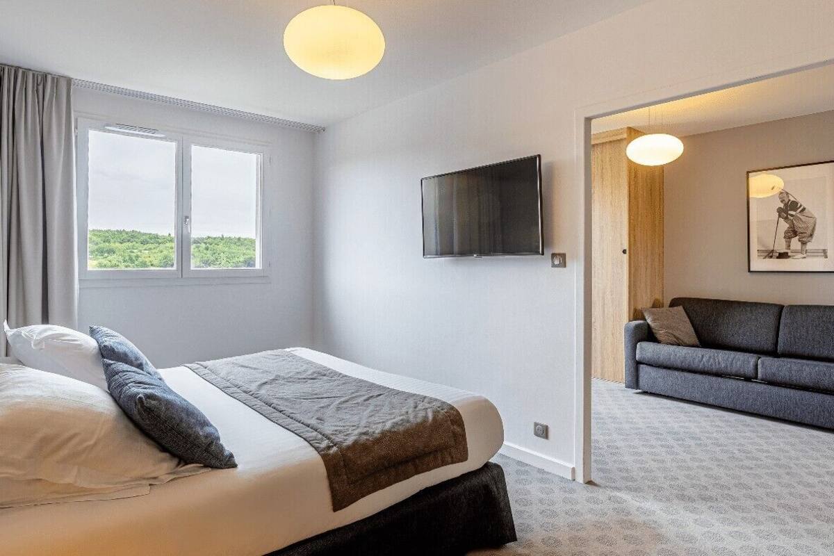 Un dormitorio con cama, televisor, sofá y un amplio ventanal.