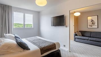 Un dormitorio con cama, televisor, sofá y un amplio ventanal.