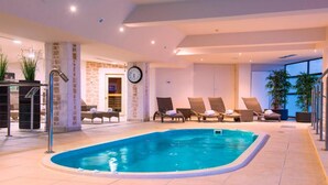 Una piscina interior con sillones de descanso y un reloj en la pared.