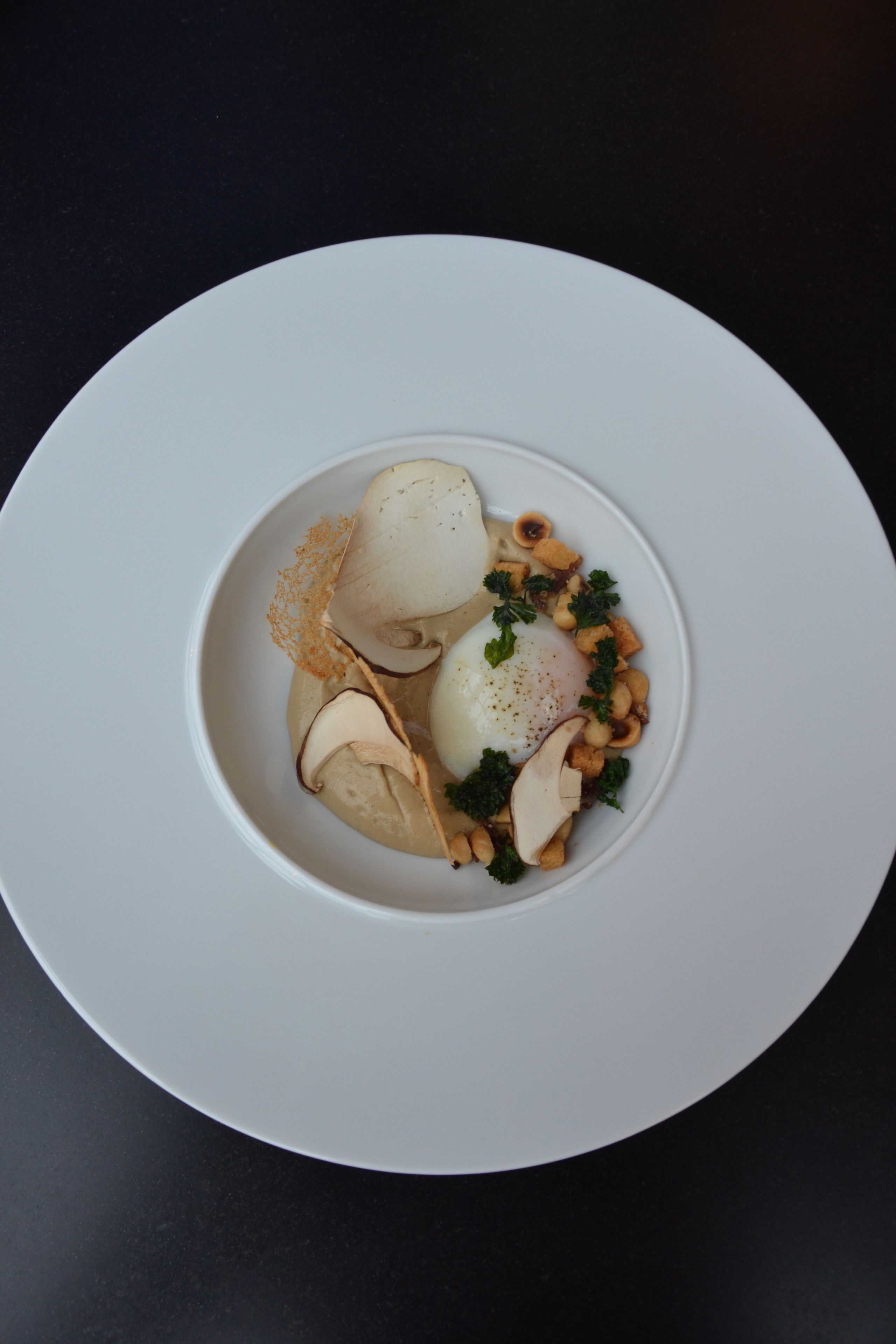 Une assiette blanche contenant un plat composé de pommes de terre en tranches, d’un œuf poché et de quelques garnitures.