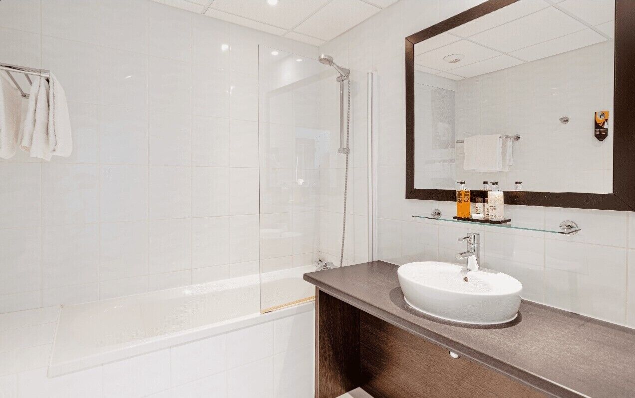 A modern bathroom with a glass-enclosed shower, a white sink, and a large mirror.
