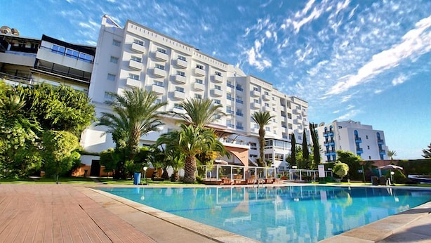 Een hotel met een zwembad, palmbomen en een helderblauwe lucht.