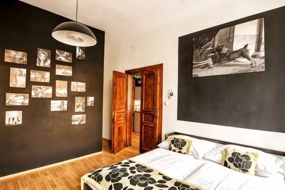 Ein Schlafzimmer mit einem Bett, einer Hängeleuchte, einer Tür und einer Wand mit gerahmten Bildern.