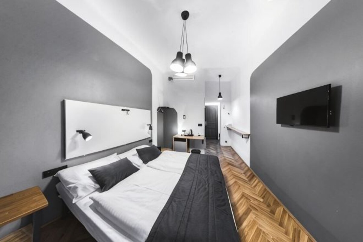 A modern hotel room with a large bed, a TV mounted on the wall, and a wooden floor.