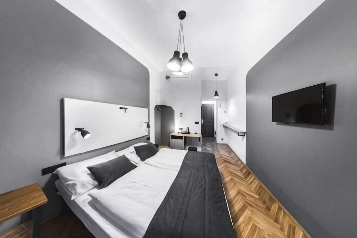 A modern hotel room with a large bed, a TV mounted on the wall, and a wooden floor.