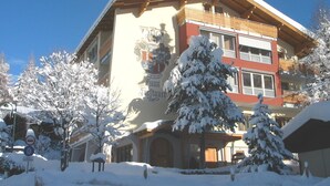 A multi-story building with a snow-covered exterior and a prominent crest on the facade. - Appartements Furstauer (Saalbach-Hinterglemm)