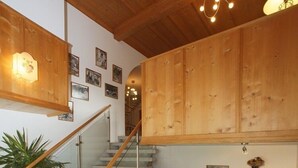 A wooden staircase with a glass railing, a lantern, and a decorative cabinet. - Appartements Furstauer (Saalbach-Hinterglemm)