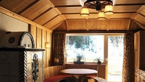 A cozy cabin interior with a wooden ceiling, a round table with benches, and a window with curtains. - Appartements Furstauer (Saalbach-Hinterglemm)