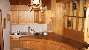 A wooden kitchen with a bar counter and stools. - Appartements Furstauer (Saalbach-Hinterglemm)
