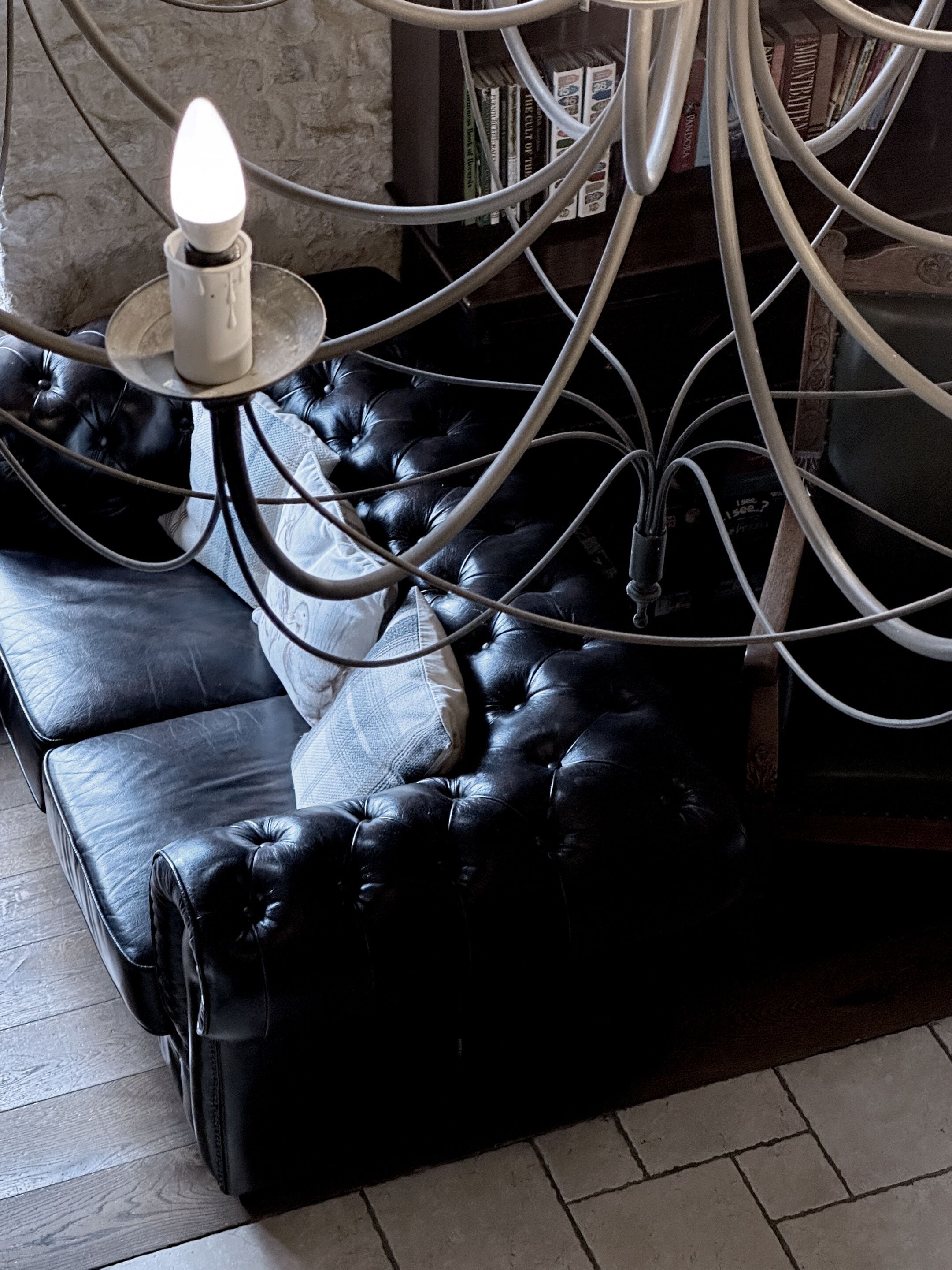 A black leather sofa with a white candle on a metal stand, surrounded by books and cables.