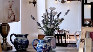A room with a table displaying ceramic pitchers, a vase with flowers, a lamp with a rabbit design, and wall sconces. - The Crown at Marnhull (Sturminster Newton)