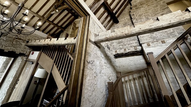 A rustic interior with exposed wooden beams, stone walls, and a chandelier. - The Crown at Marnhull (Sturminster Newton)