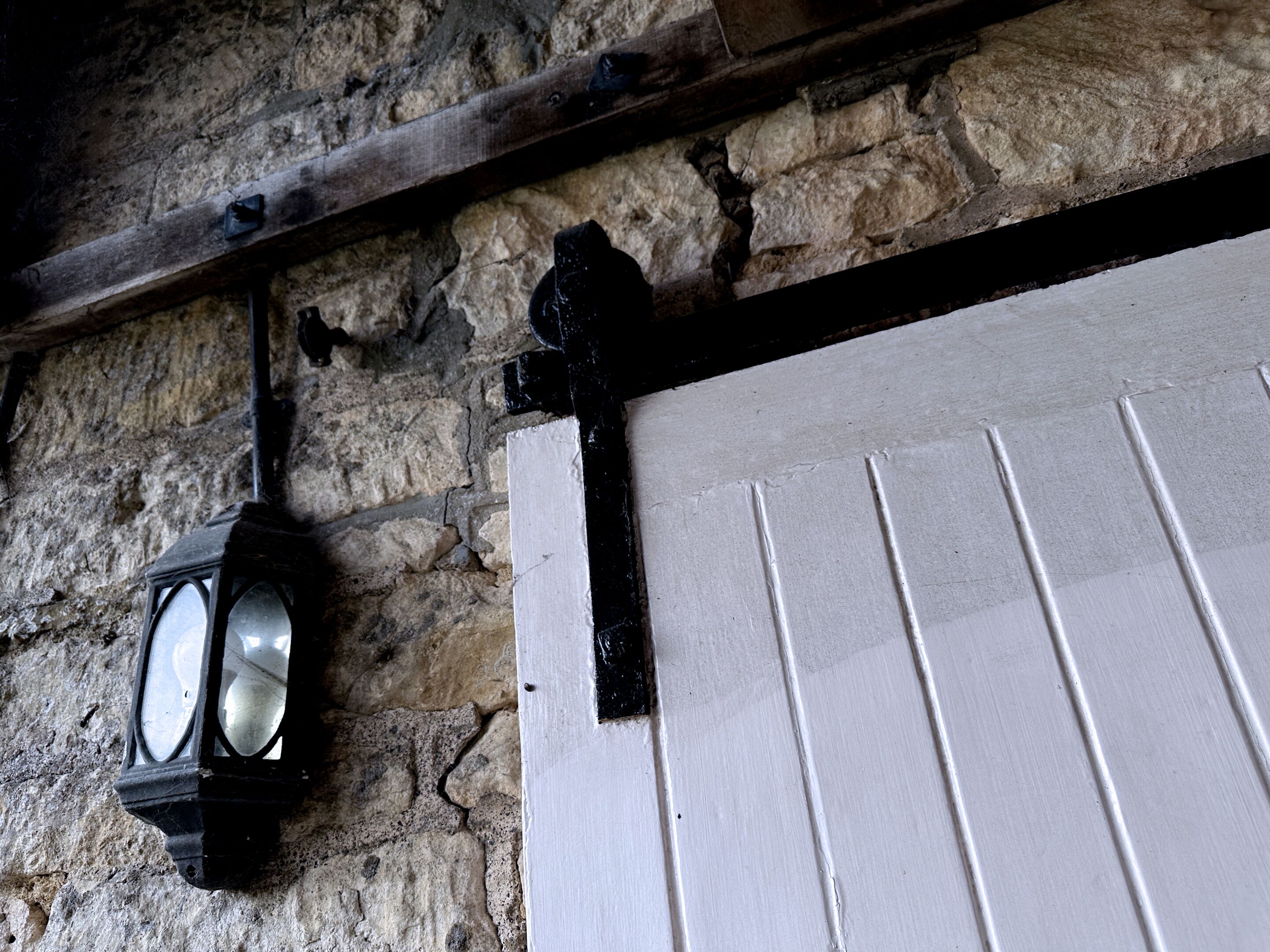 A stone wall with a wooden beam and a white door with black trim.