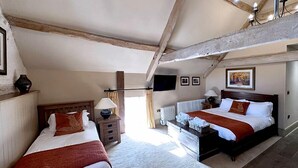 A bedroom with two beds, a dresser, a radiator, and a TV on the wall. - The Crown at Marnhull (Sturminster Newton)
