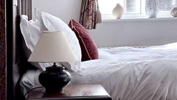 A neatly made bed with white linens, a dark wooden nightstand with a lamp, and a window with curtains.