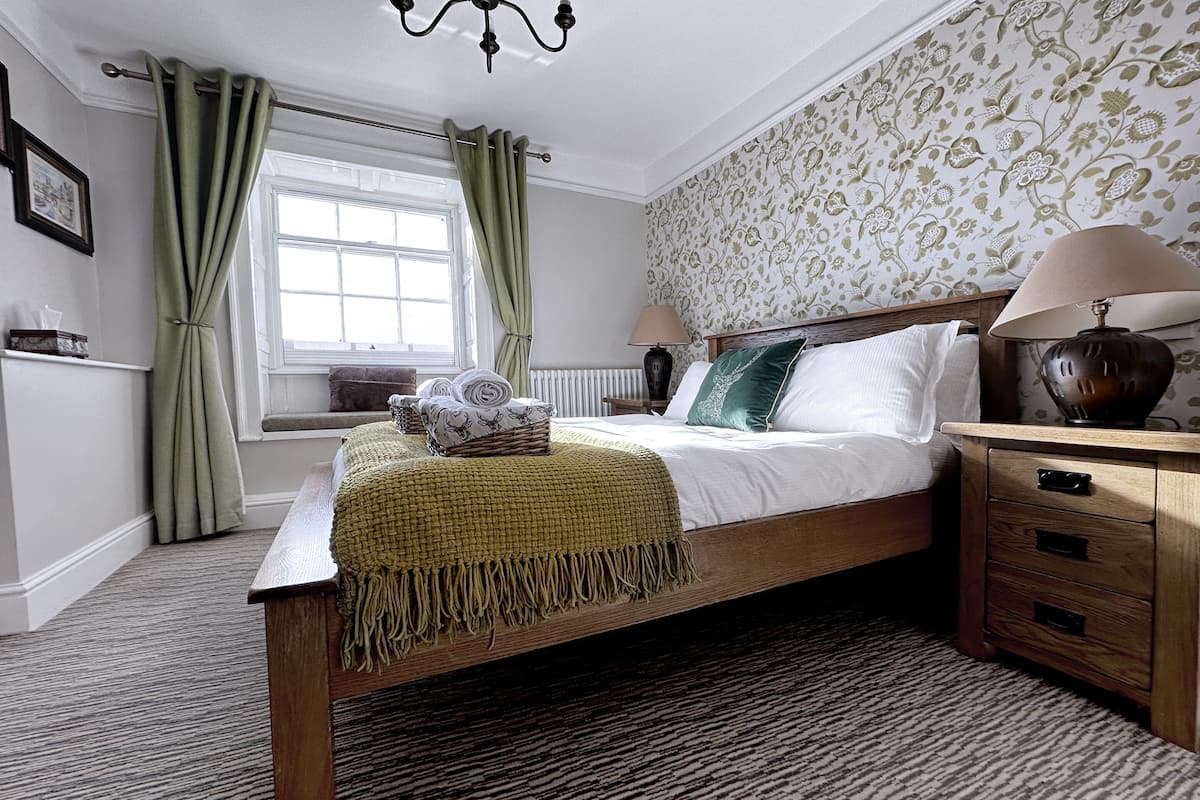 A neatly arranged bedroom with a wooden bed, a bedside lamp, and a window with curtains.