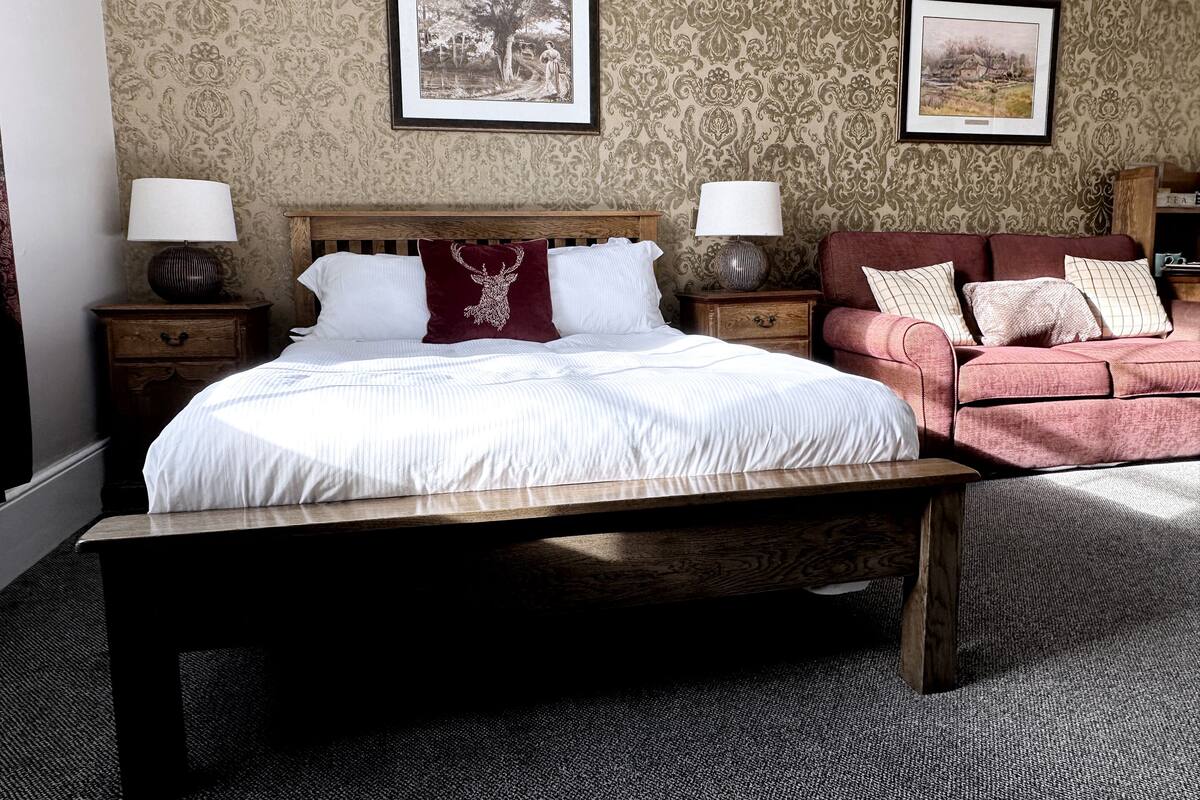 A bedroom with a large bed, two bedside tables, a wooden bench, a red sofa, and two framed pictures on the wall.