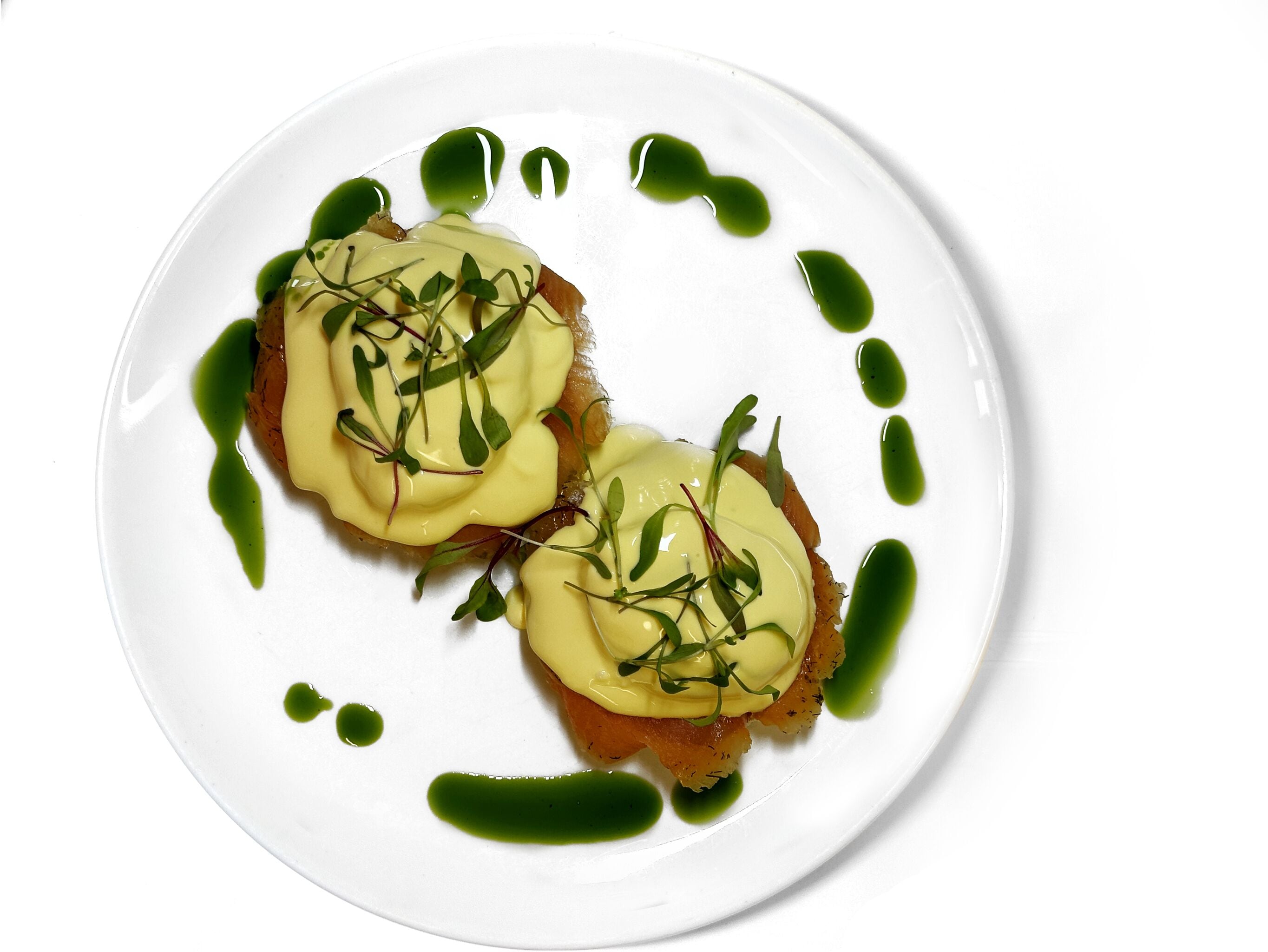 A white plate with two pieces of food topped with green sauce and greens.