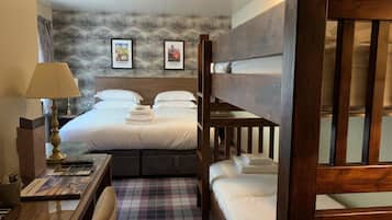 A hotel room with a bunk bed, a desk with a lamp, a checkered floor, and framed pictures on the wall.