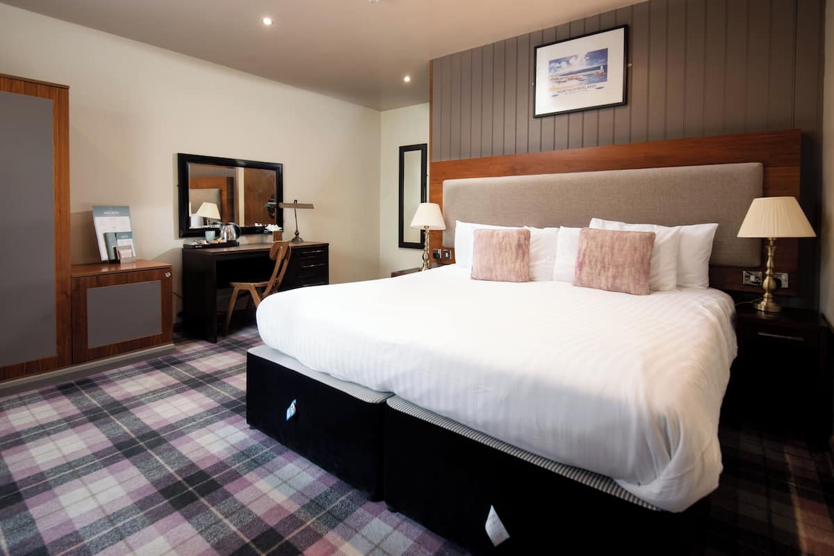 A hotel room with a large bed, a desk with a chair, a dresser, and a mirror.