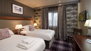 Une chambre d’hôtel avec deux lits, une tête de lit en bois, une moquette à carreaux et un bureau avec une chaise.