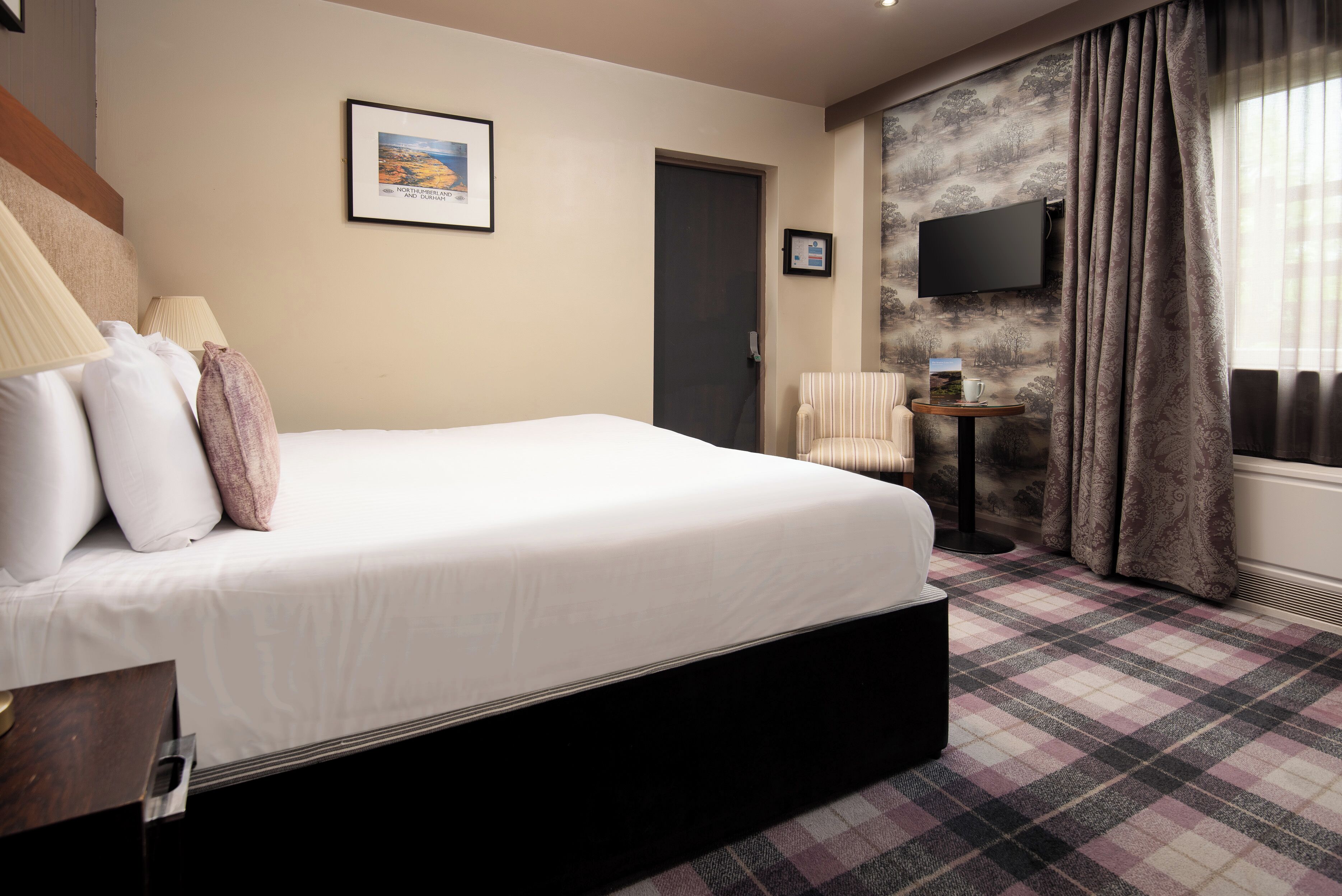 A hotel room with a bed, a chair, a small table, a TV, and a door.