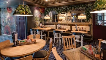 Un restaurante con mesas y sillas de madera, decoración floral en la pared y lámparas colgantes.