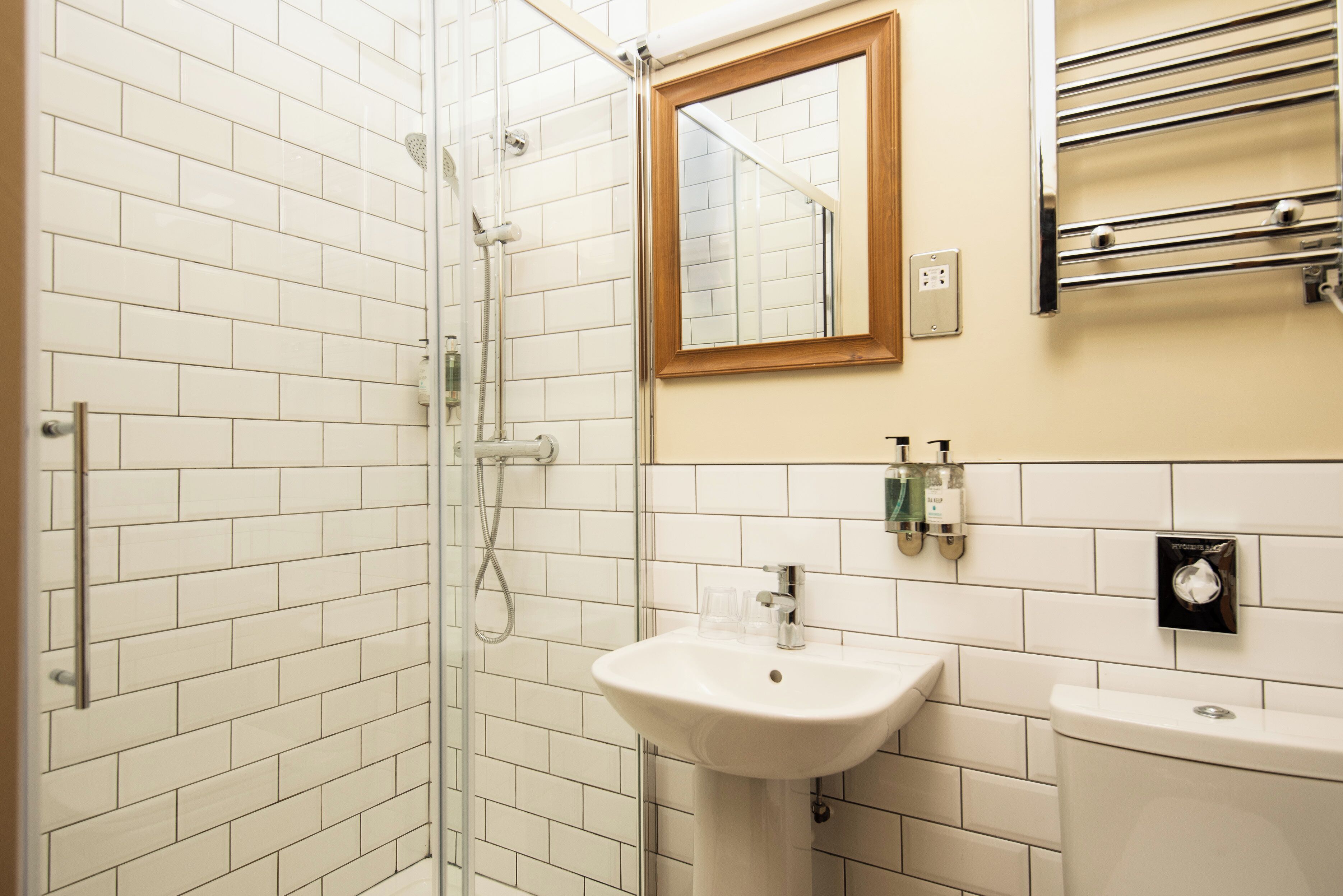 Een badkamer met witte betegelde wanden, een glazen douchecabine, een wastafel en een spiegel.