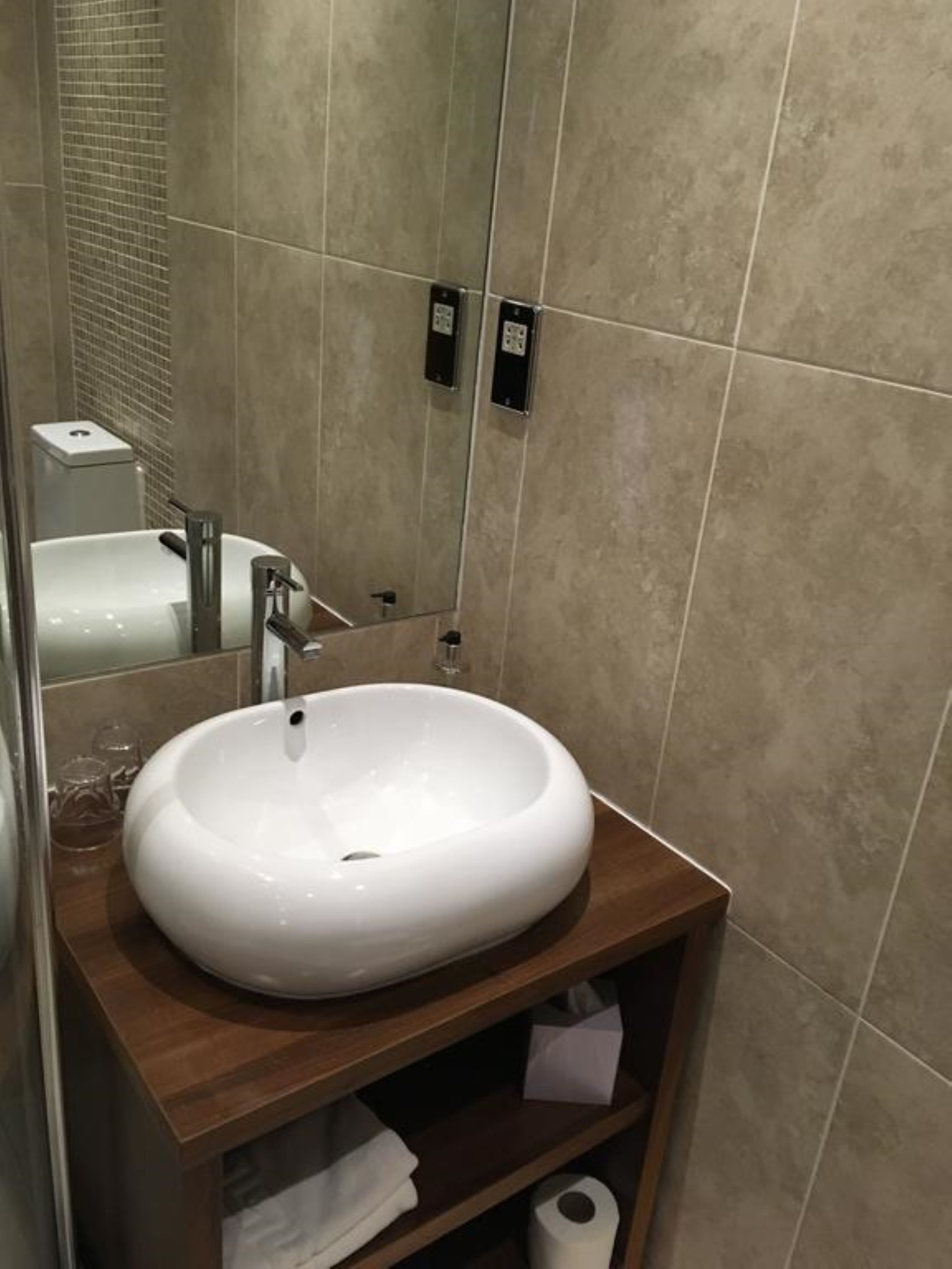 A bathroom with a white sink, wooden vanity, and a mirror.