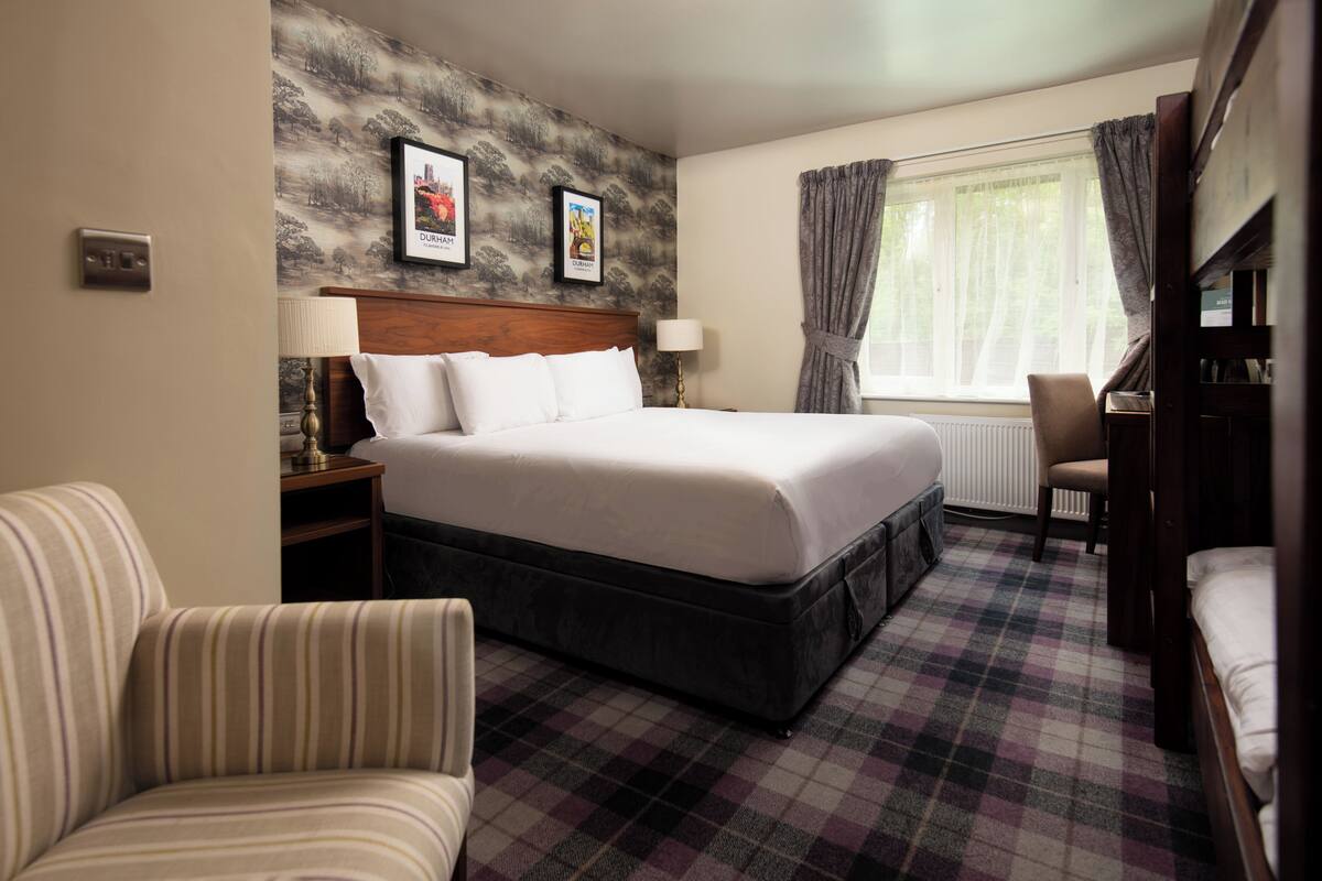 A hotel room with a large bed, a chair, a desk, and a window with curtains.