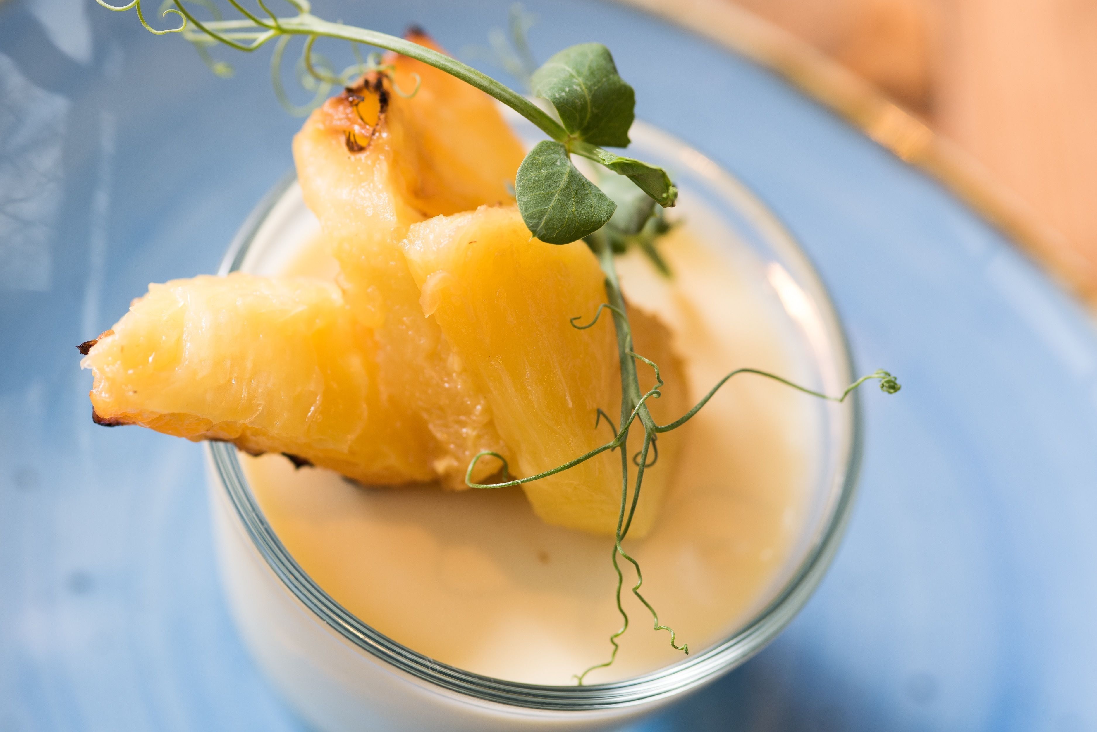 Un recipiente de vidrio para postre con trozos de piña y una ramita de hojas verdes.