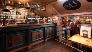 Un espace bar avec un comptoir en bois, des étagères remplies de bouteilles et un panneau indiquant où commander de la nourriture et des boissons.