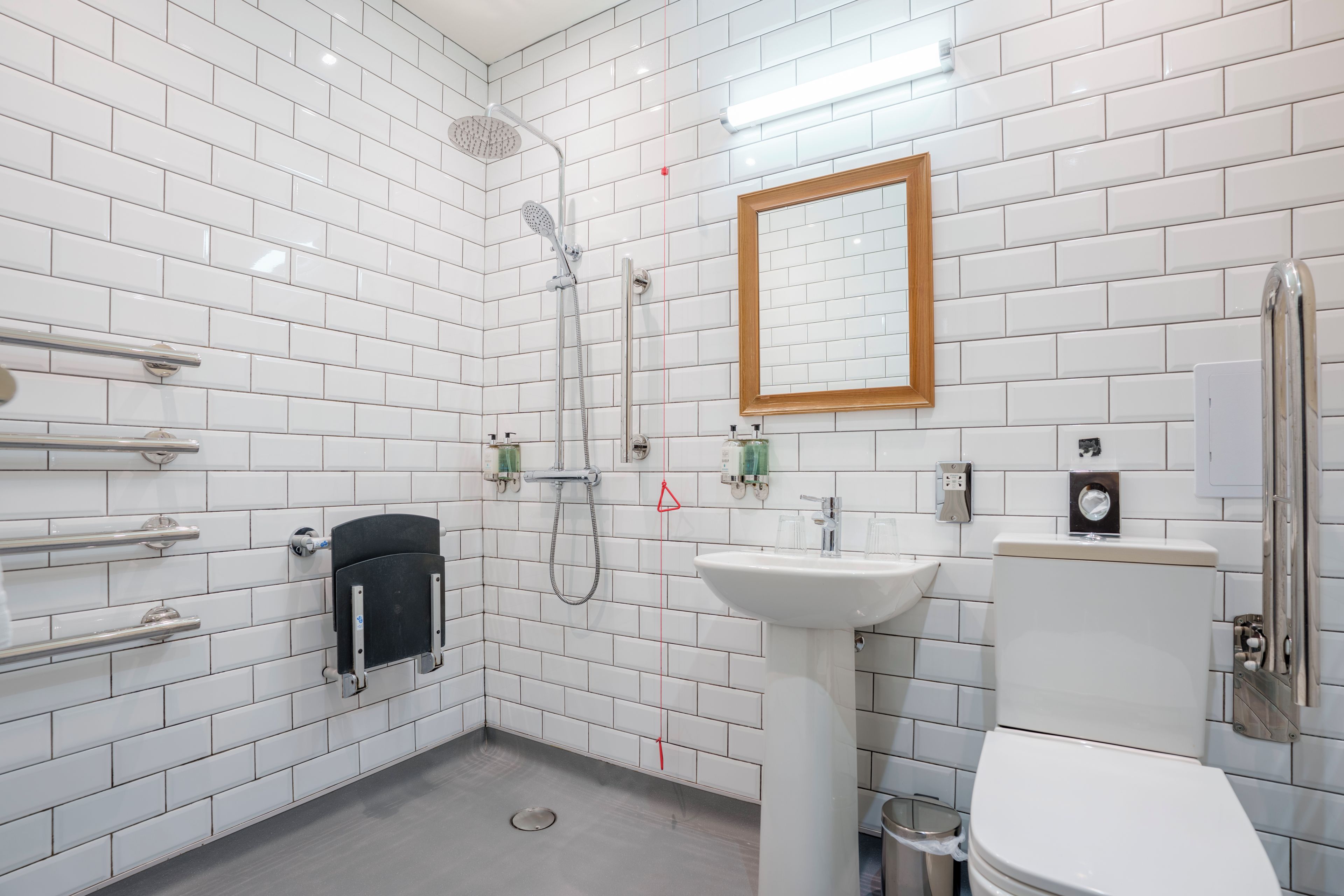 Un baño pequeño y moderno con azulejos blancos tipo metro, un lavamanos blanco, un inodoro y una ducha con cabezal de ducha manual.