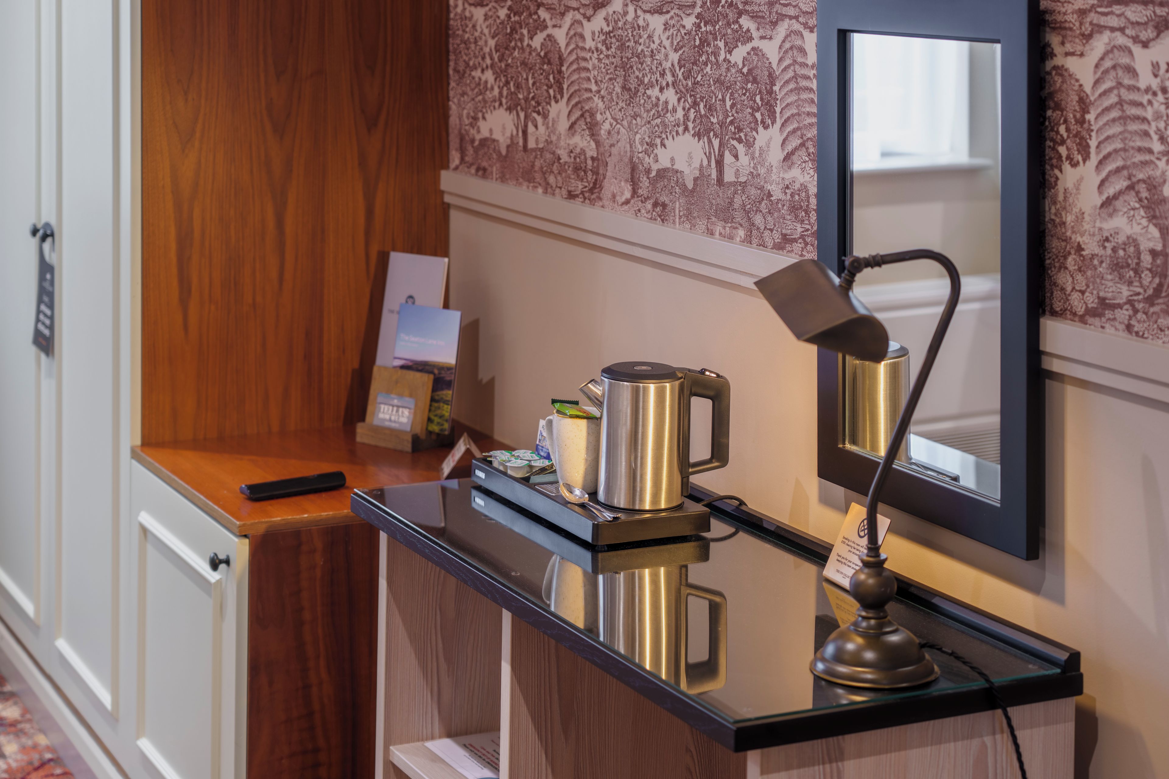 A hotel room with a minibar, a coffee maker, a lamp, and a mirror.