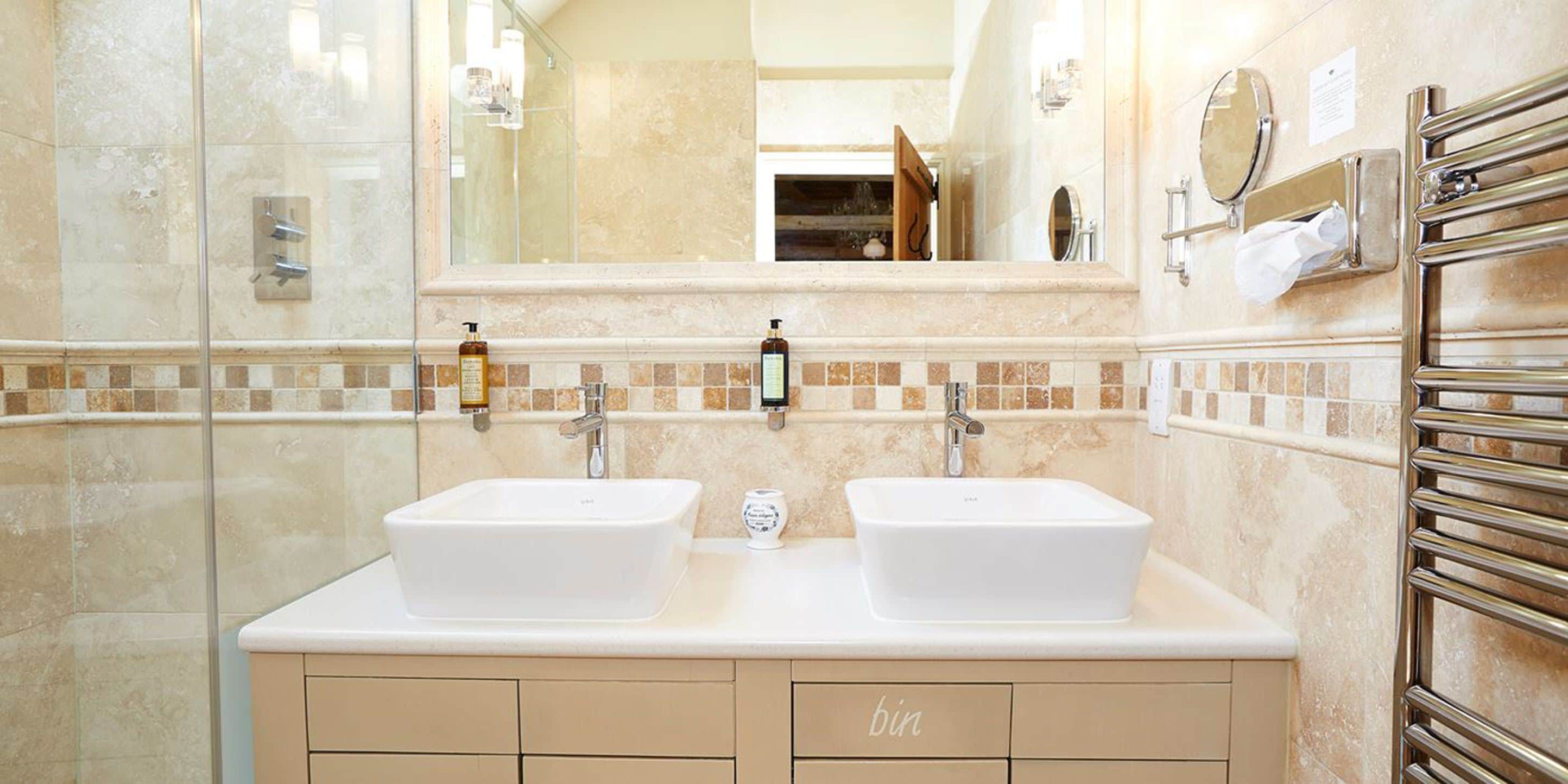 A modern bathroom with two sinks, a glass shower enclosure, and a vanity with a mirror and towel rack.