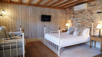 A bedroom with a white metal bed, a wooden ceiling, a brick wall, a television mounted above the bed, and two bedside lamps.