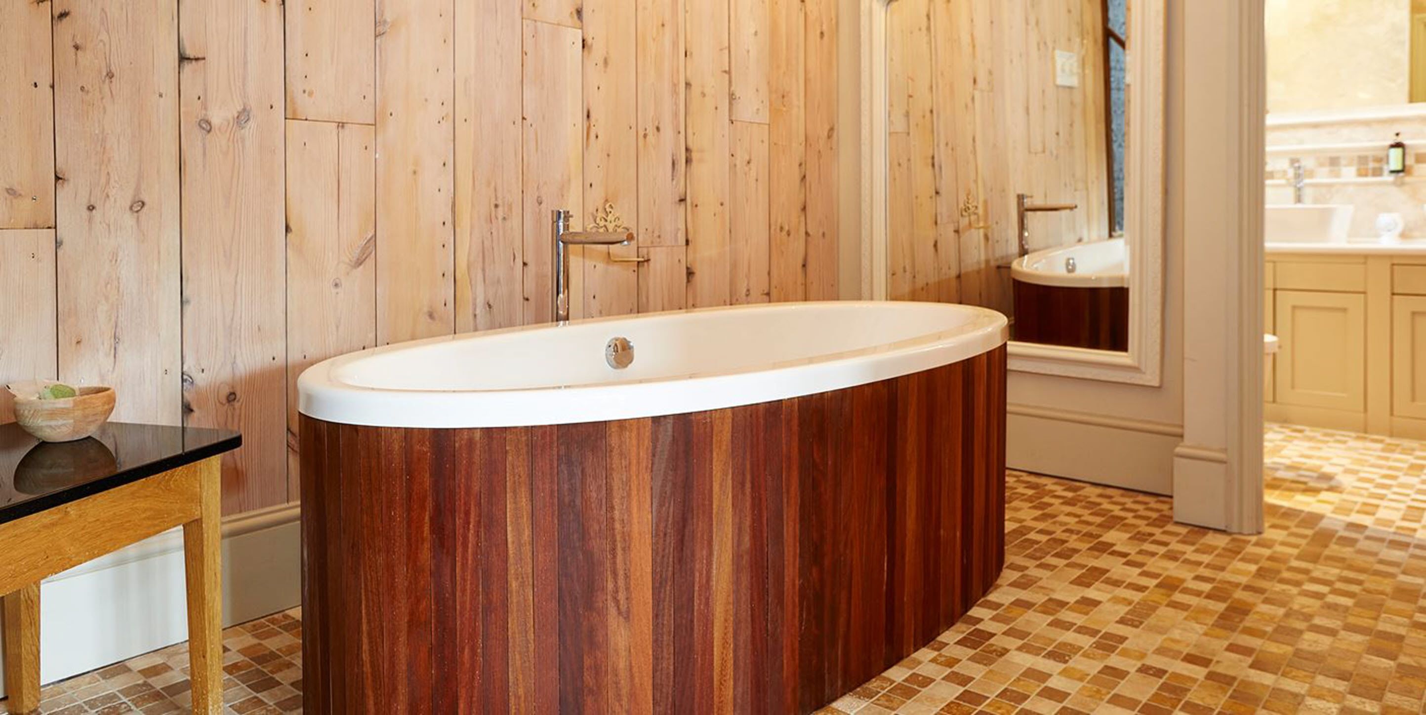 A bathroom with a wooden panel wall, a freestanding bathtub, a sink, and a tiled floor.