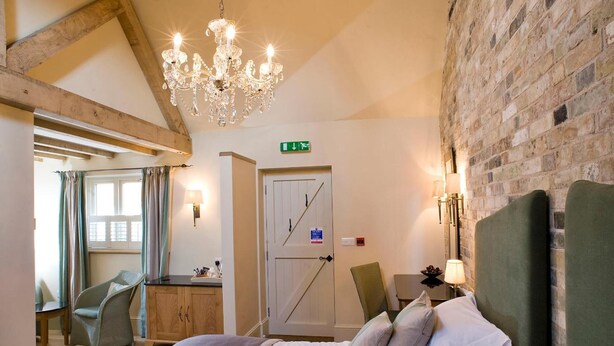 A bedroom with a bed, a chandelier, a brick wall, and a wooden ceiling. - The Fox Inn by Greene King Inns (Bury St Edmunds)