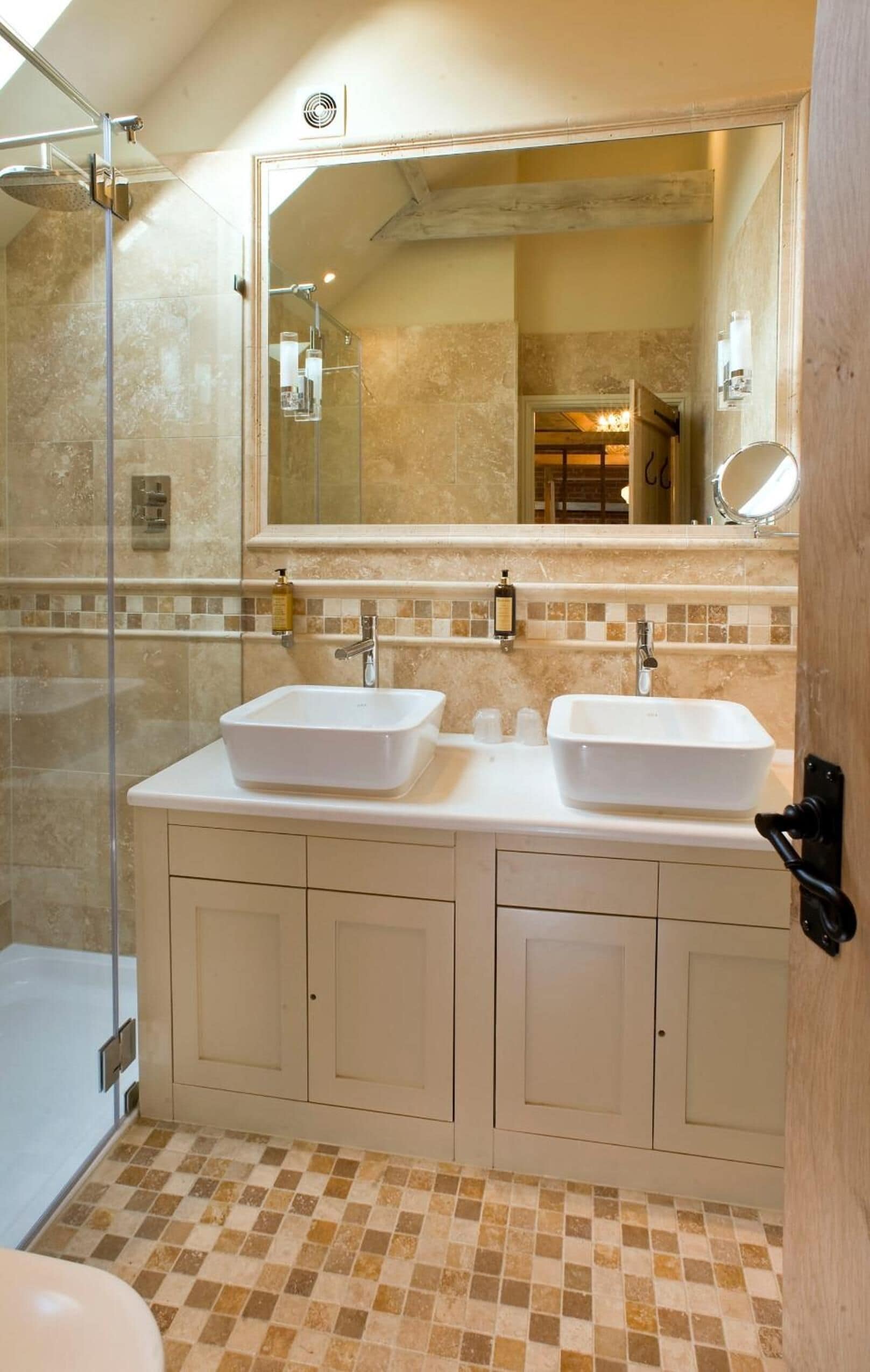 A bathroom with two sinks, a glass shower enclosure, and a tiled floor.