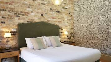 A neatly made bed with a green headboard, two bedside lamps, and a brick-patterned wall.