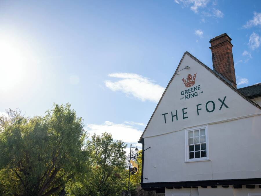 Een gebouw met een bord waarop 'GREENE KING 1799 THE FOX' staat, en een kroon erboven.