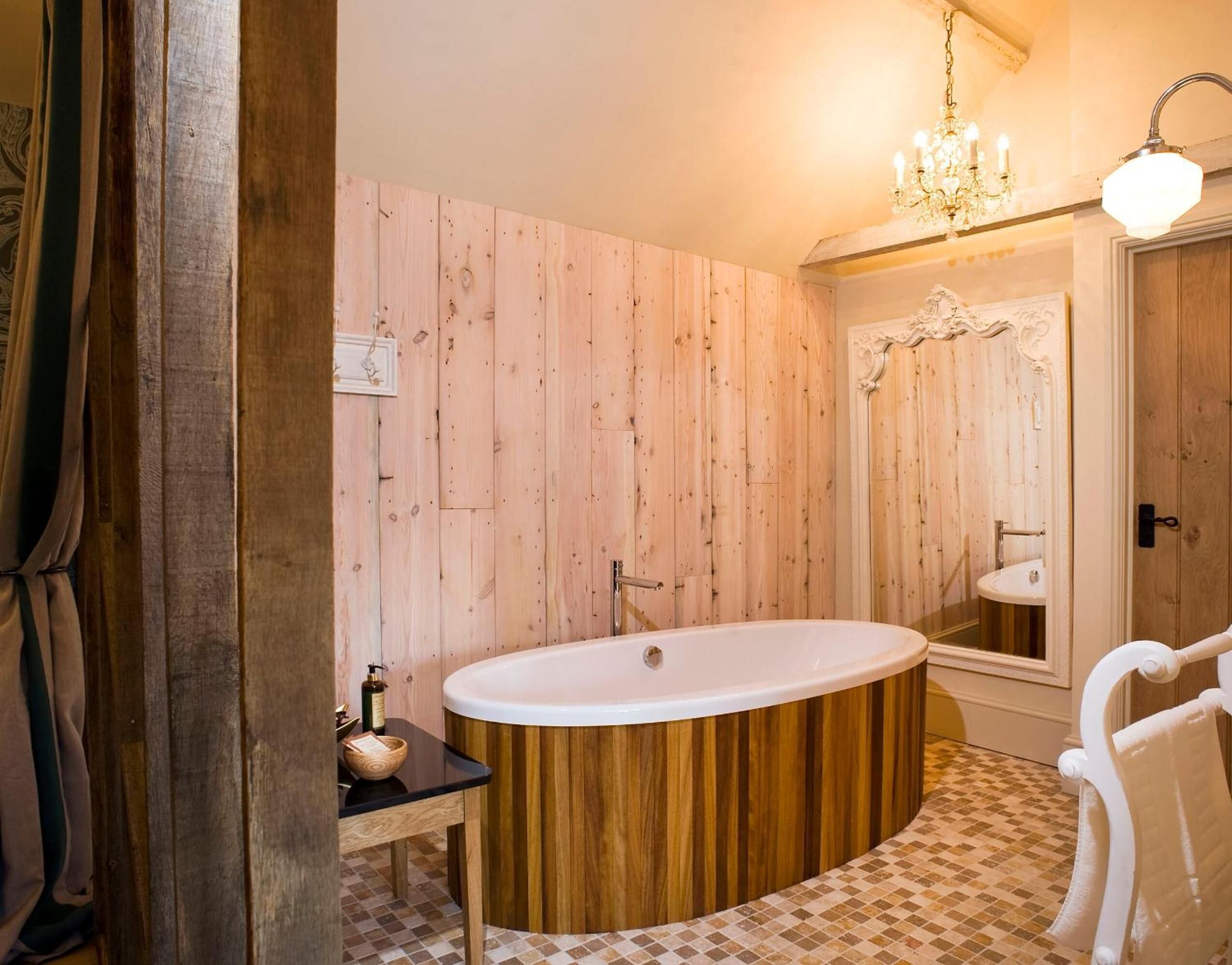 Un bagno con rivestimento in legno, una vasca da bagno indipendente, un lavabo e un lampadario.
