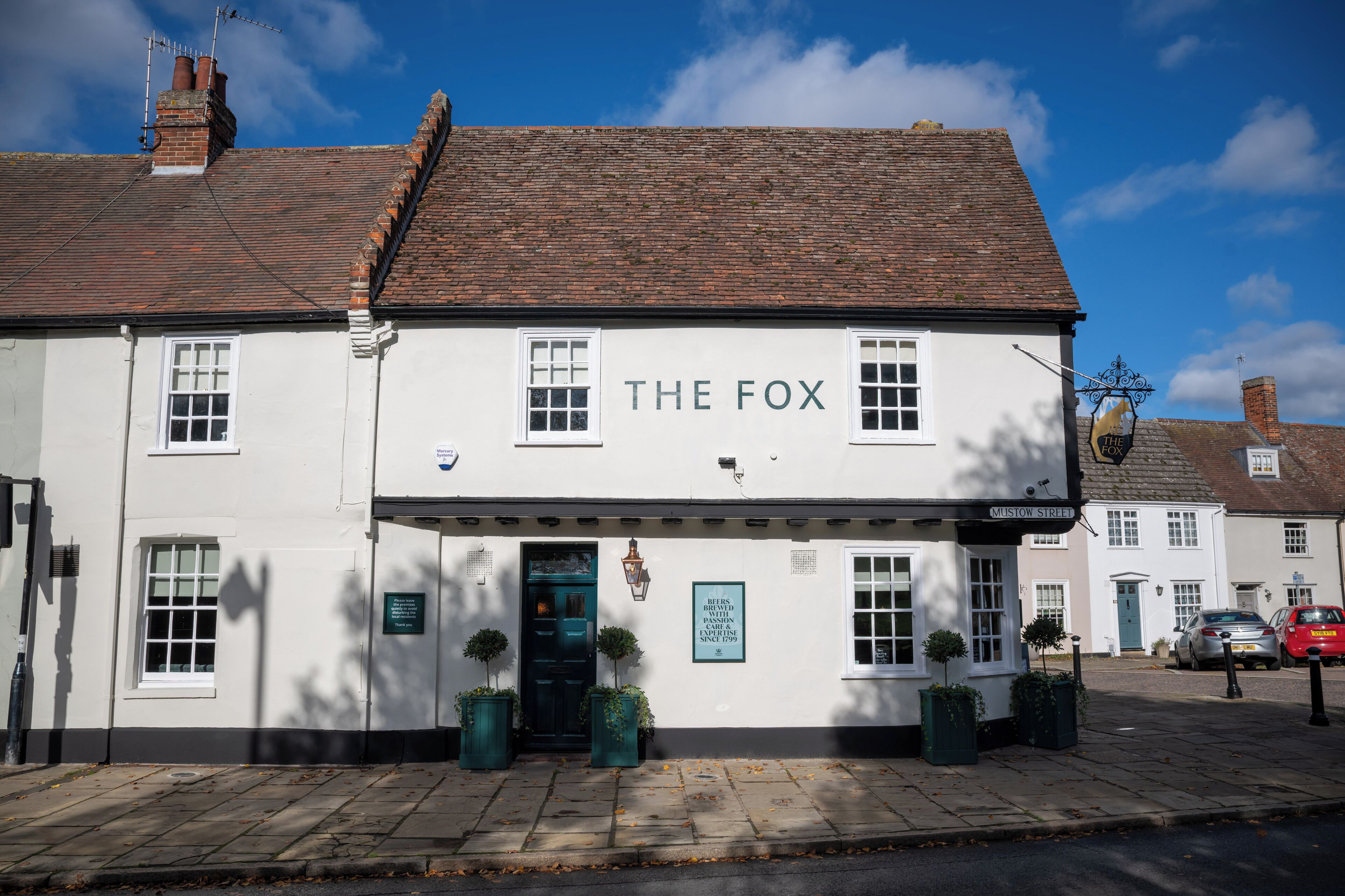 A traditional pub named "The Fox" with a classic brick facade, a green door, and a signboard indicating its location on Mustow Street.