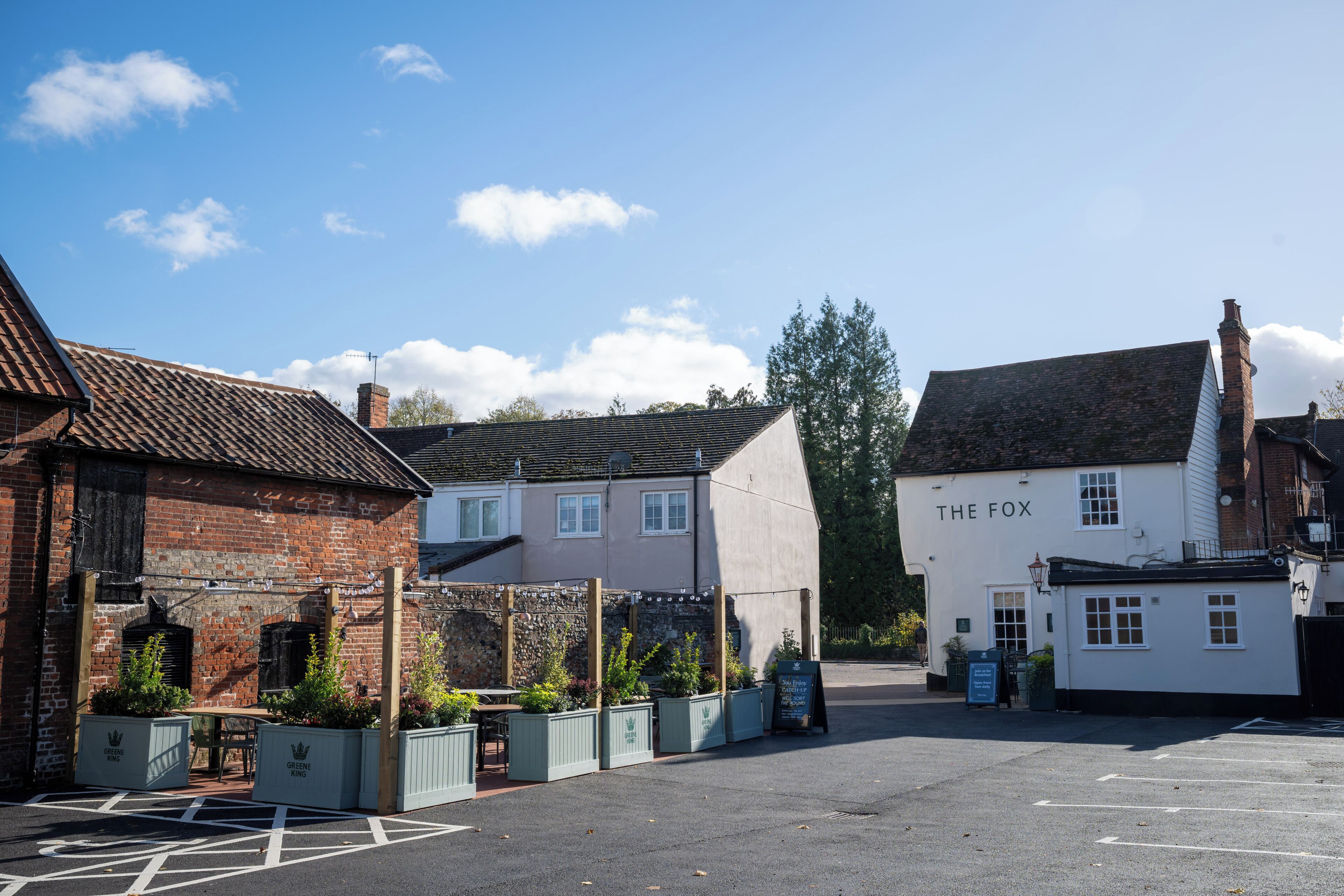 Un pub traditionnel appelé « The Fox », avec une façade en briques et un extérieur blanc, entouré d’un parking et de verdure.